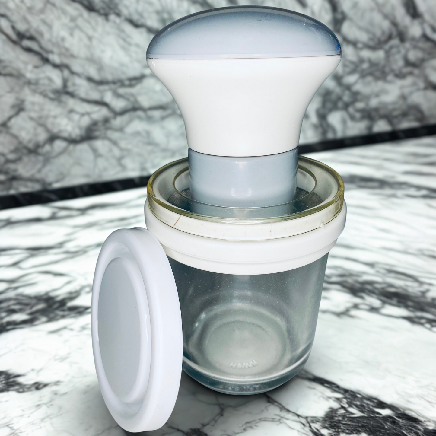 Weiße Safran Reibe mit Glasbehälter und Deckel auf einer Marmortischplatte, minimalistisches Produktfoto von Safranya.