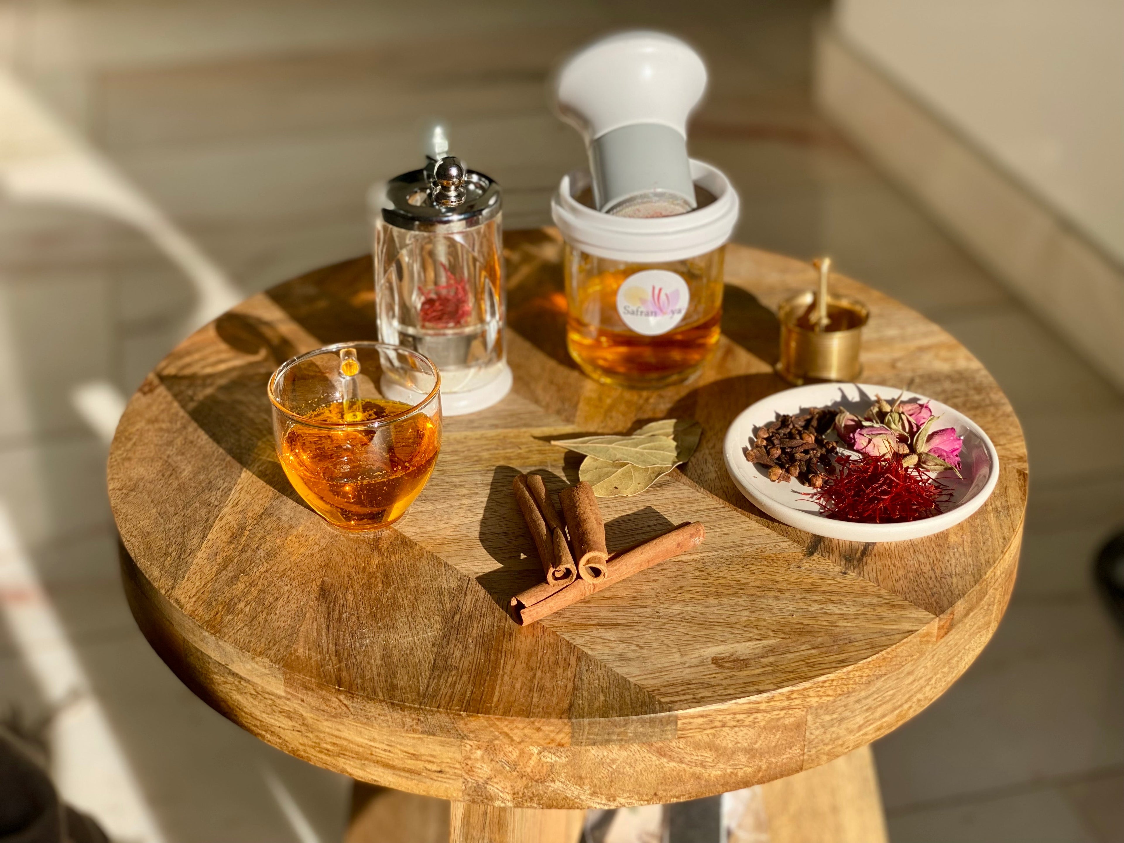 Safran Zubehör mit Safranmühle und Safranreibe auf Holztisch, daneben Glas Safrantee, Zimt, Lorbeer, Nelken, Rosenknospen und Safranfäden