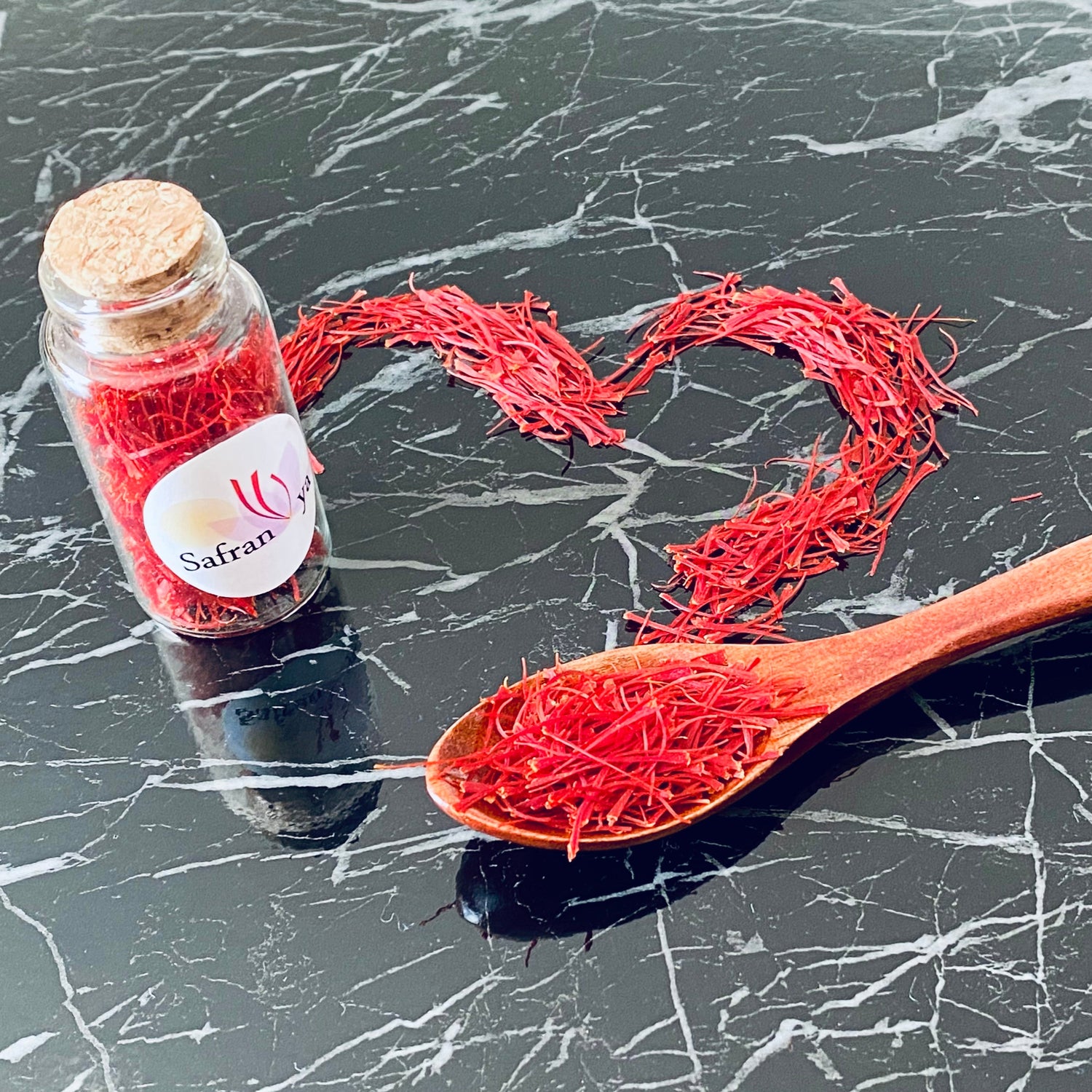 Glas mit roten Safranfäden und Herz aus Safran auf schwarzem Marmortisch – Safranya Premium Safran